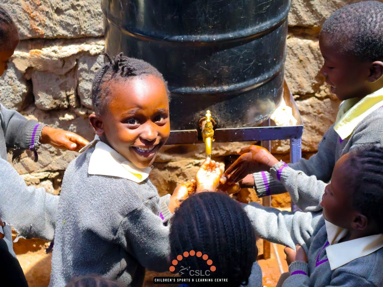 Schoolchildren washing their hands together at an outdoor water station