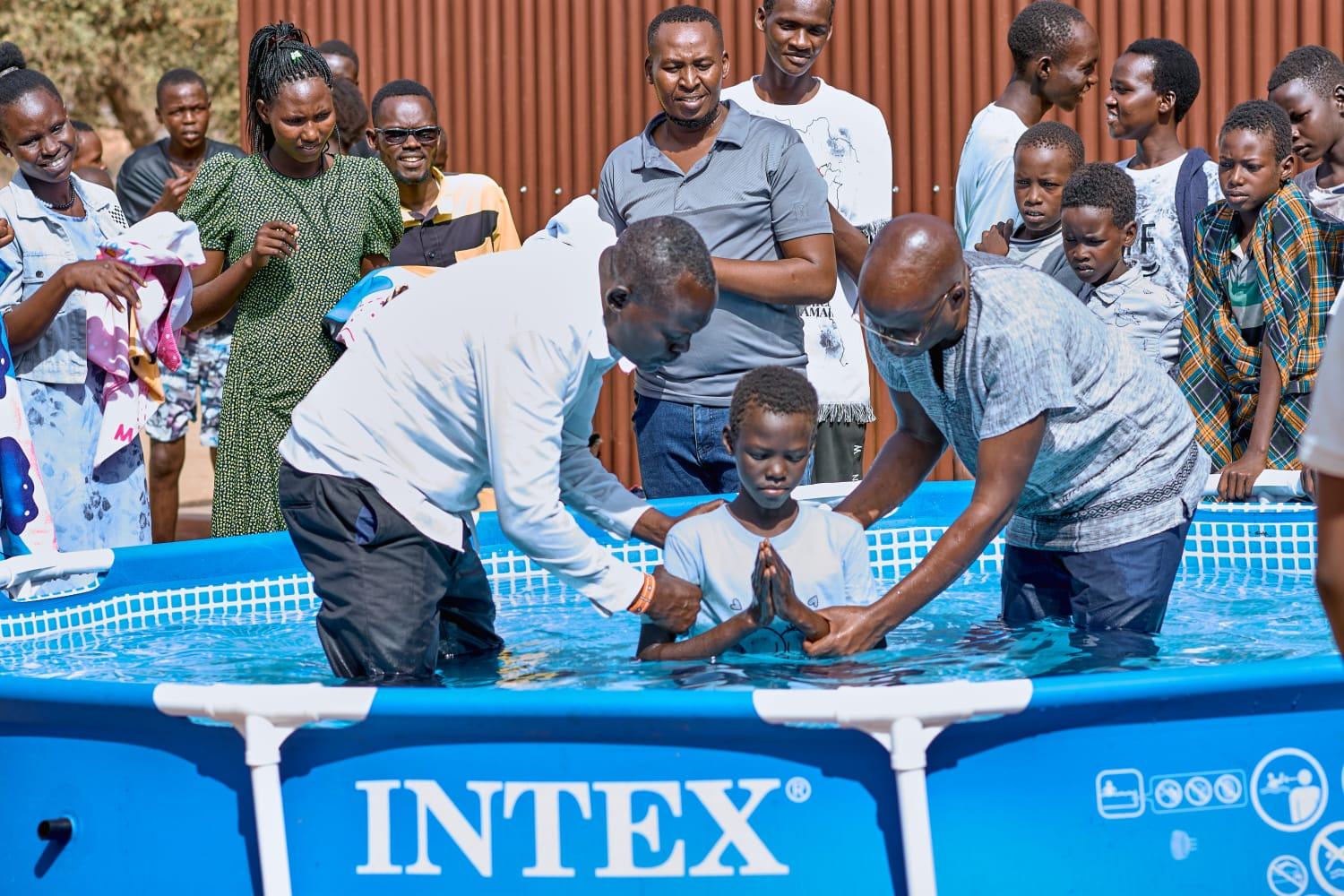 A child praying during a baptism as the community looks on