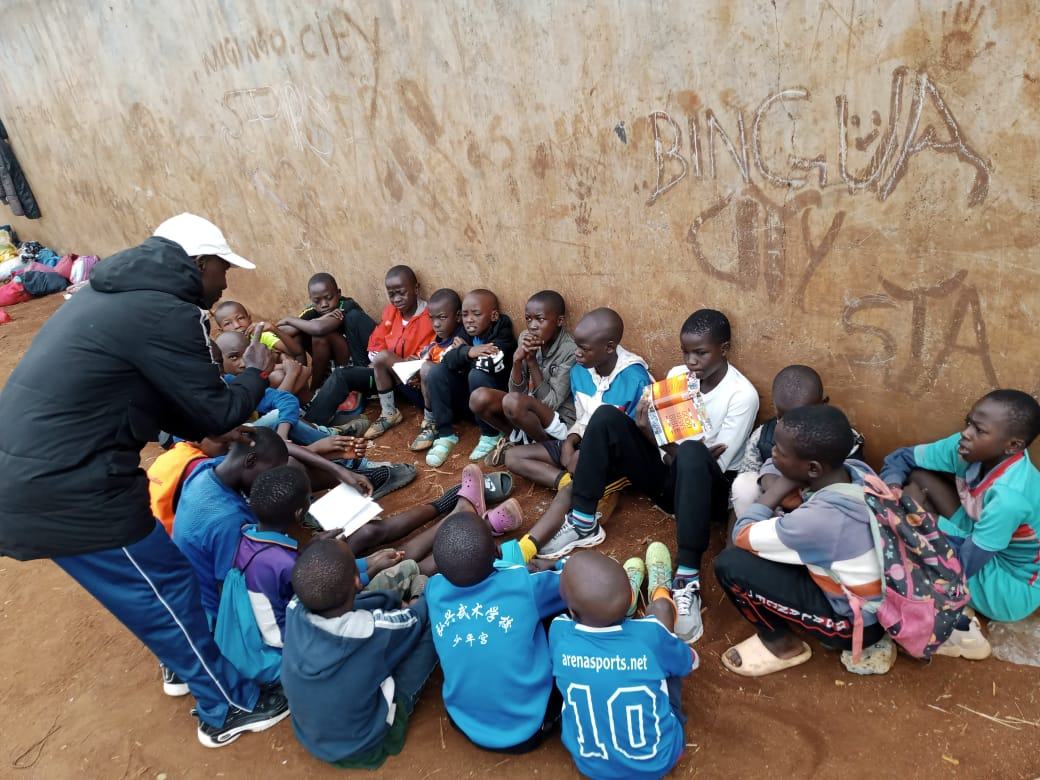 A ministry leader teaching a group of boys seated together outdoors, several holding booklets