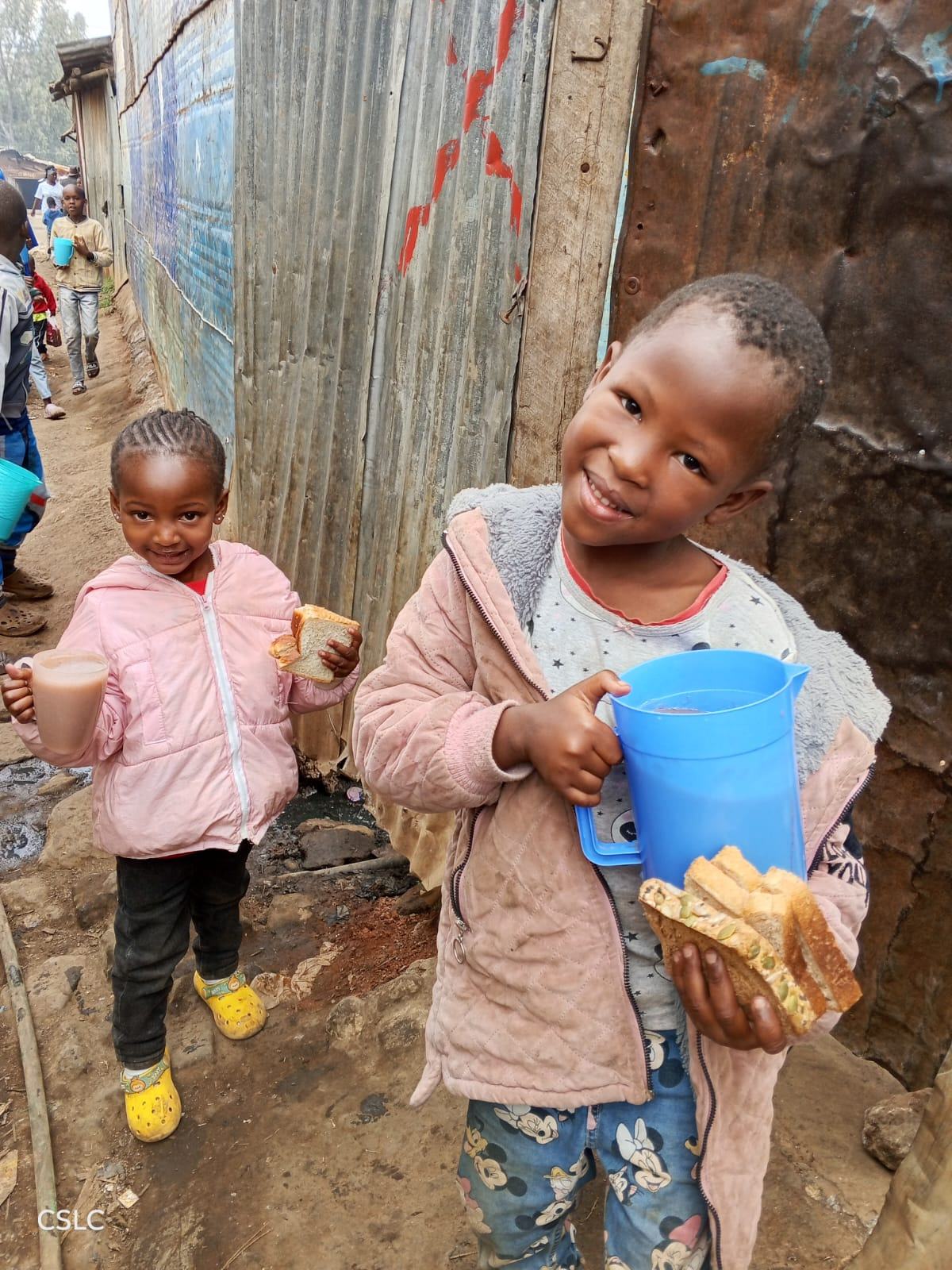 Two young children holding cups of porridge and bread in the neighborhood
