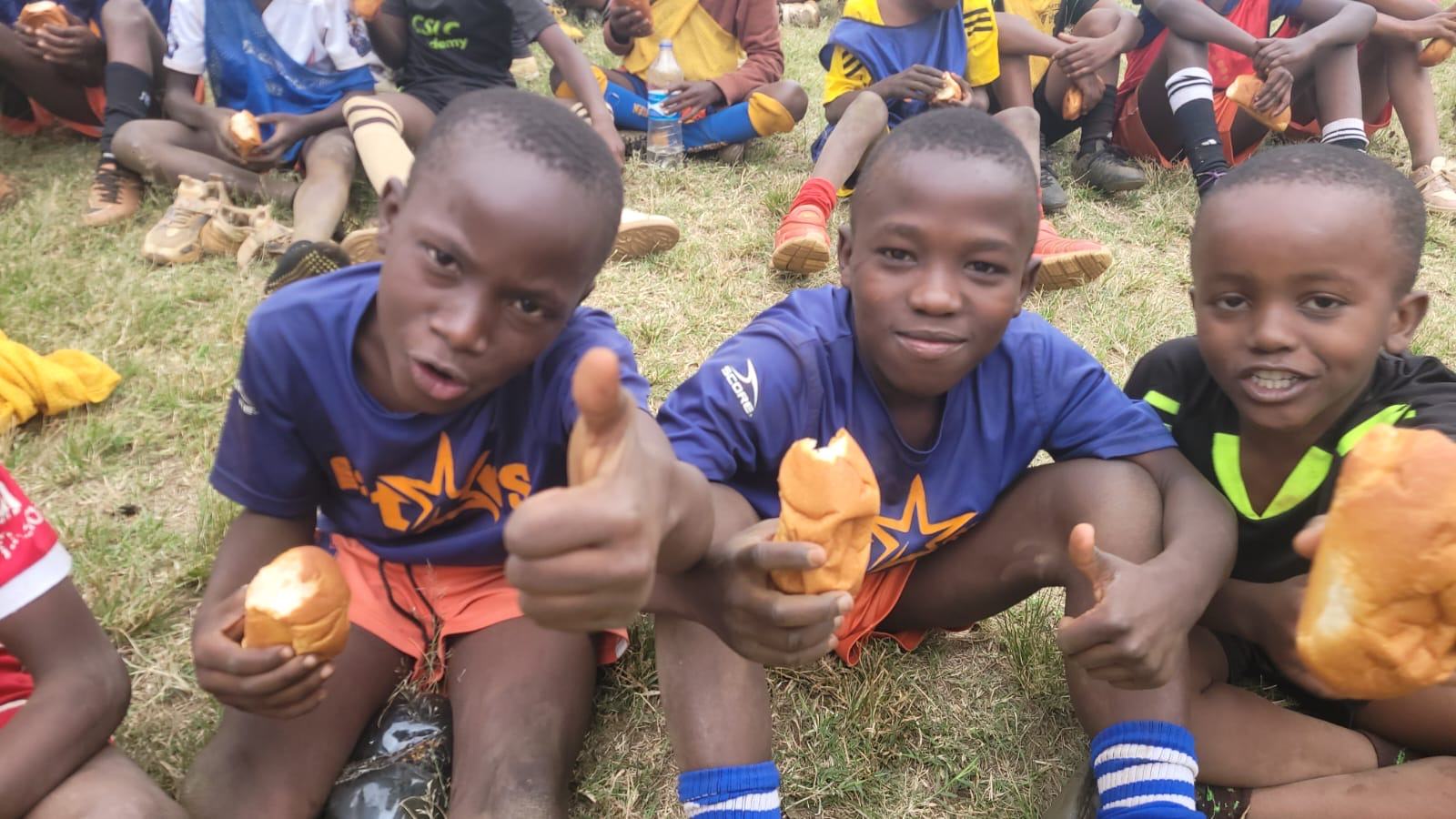 Boys giving a thumbs up while sharing bread after a match