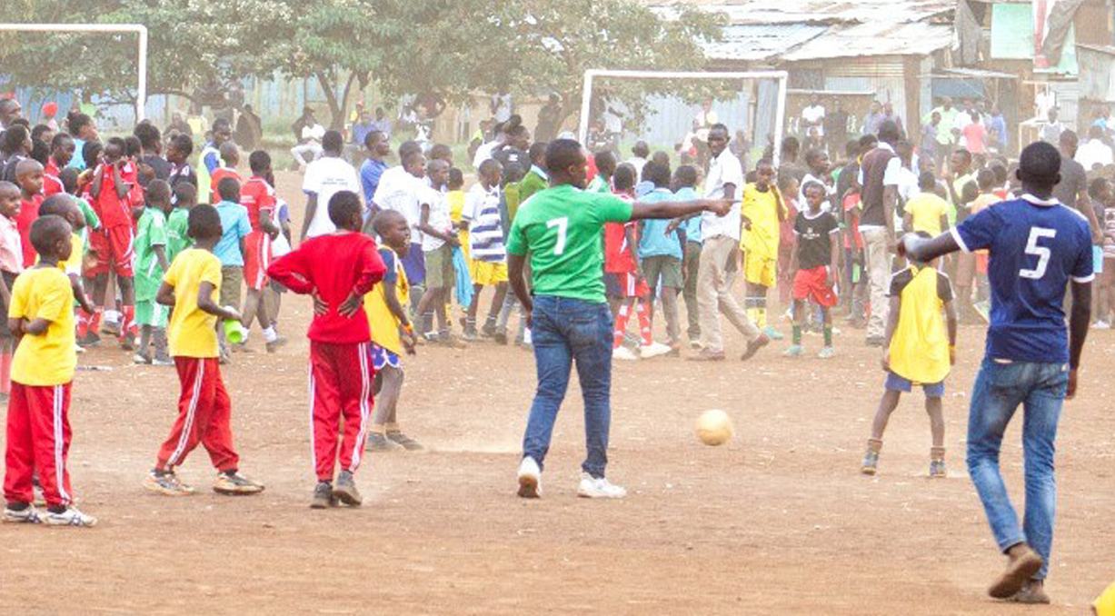 A large crowd of children in colorful jerseys playing soccer on a dirt field